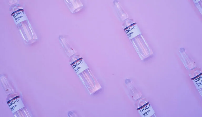 Multiple vaccine vials with COVID-19 labels arranged on a purple background