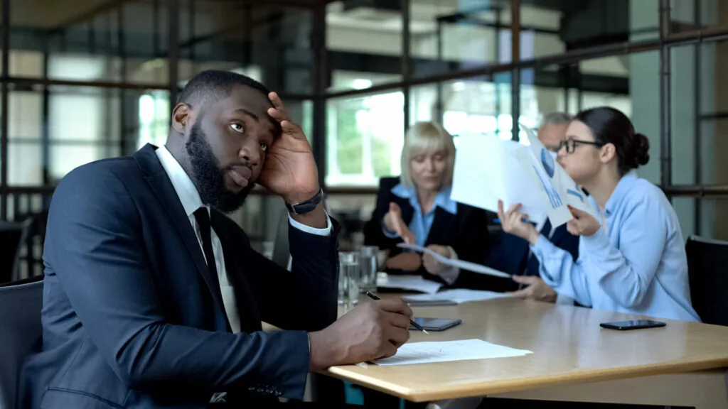Businessman looking bored or frustrated during a business meeting in a modern office conference room.